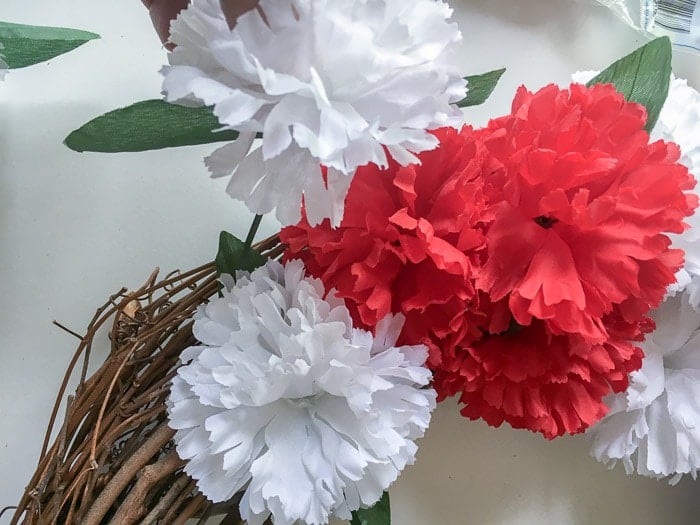 Adding flowers to the grapevine wreath form to make a red white and blue patriotic wreath