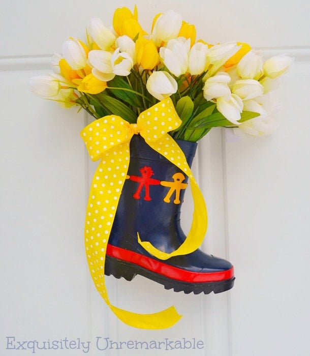 rainboot filled with faux flowers and a yellow ribbon