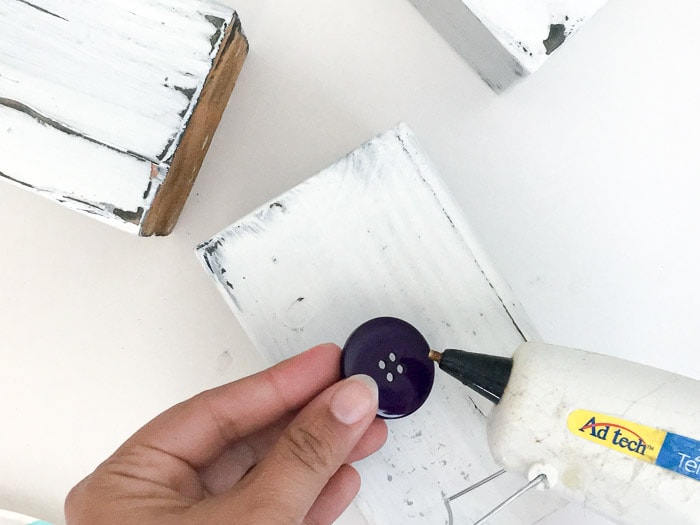 Hot glueing buttons on wood block snowman
