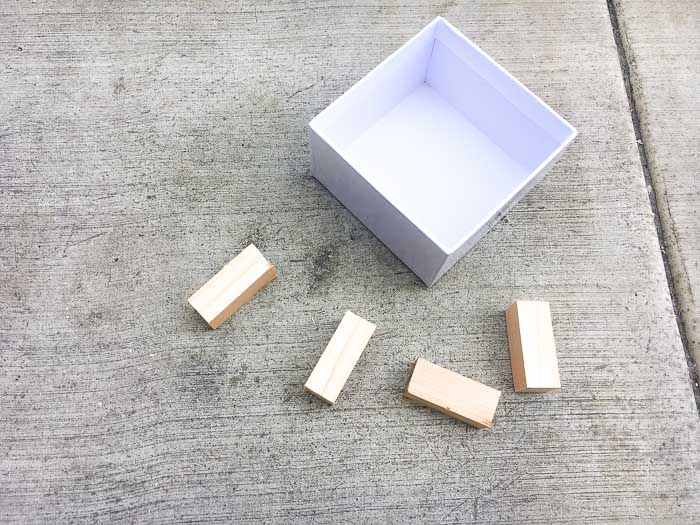 4 square dowel pieces and a cardboard box used to make a DIY concrete planter with wood feet
