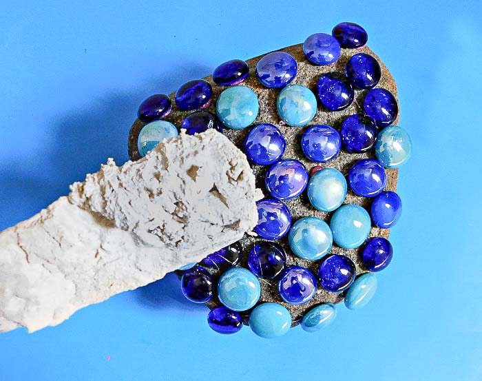 Applying grout over gems to create a mosaic rock