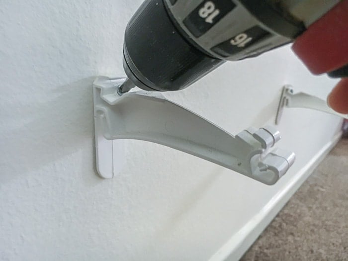 Screwing the rain gutter hangers into the wall using a power drill.