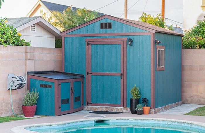 Full shed after the makeover - teal with brown trim and a few potted plants.