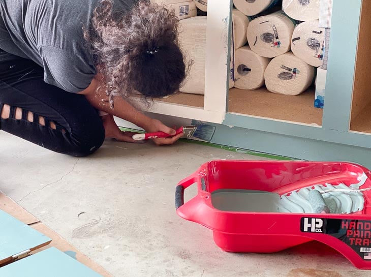 woman painting toe kick of the veneer cabinets