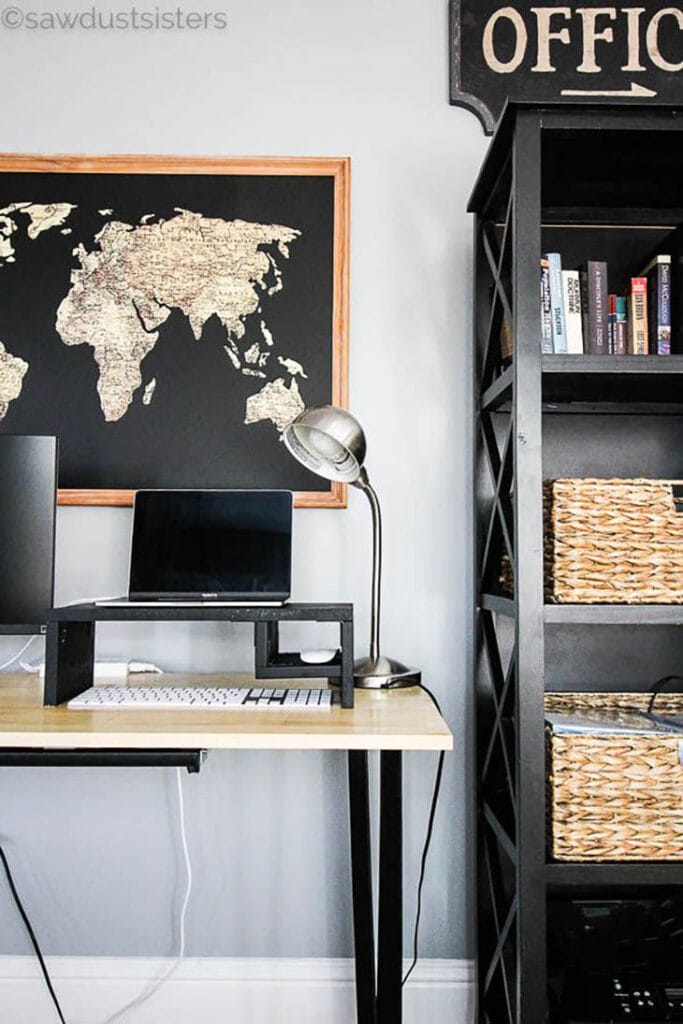Black painted DIY laptop riser with laptop on it and world map on the wall behind it