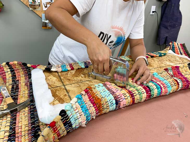 Woman attaching fabric to make the upholstered top of the shoe storage bench