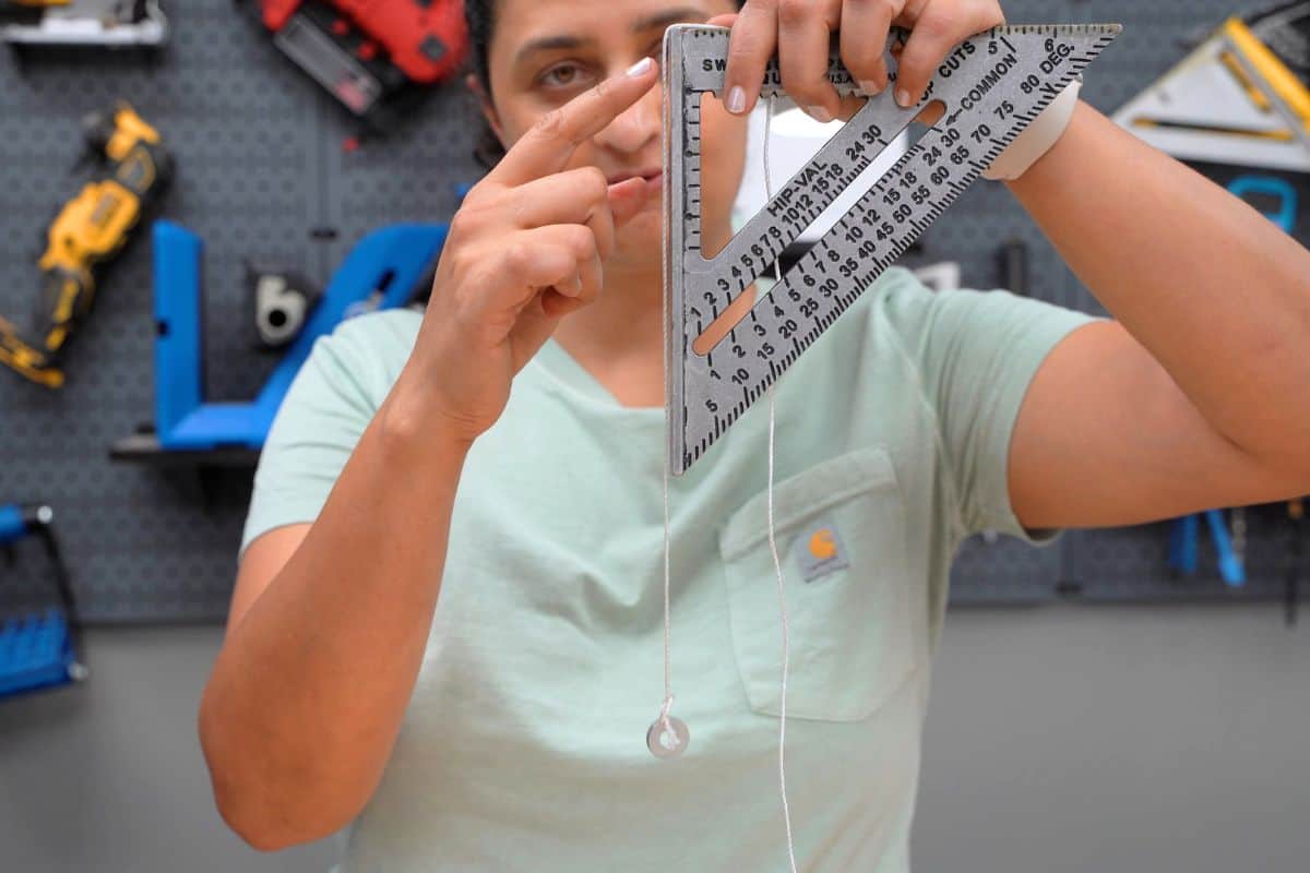 Anika holding speed square and showing how to use a string and nut on a speed square to check for level.