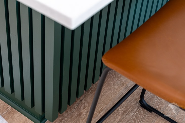 close up of dark green kitchen island with brown counter chairs