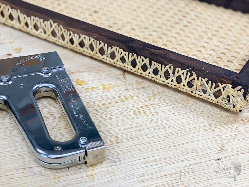 close up of all the staples holding the cane webbing to the brown wooden frame