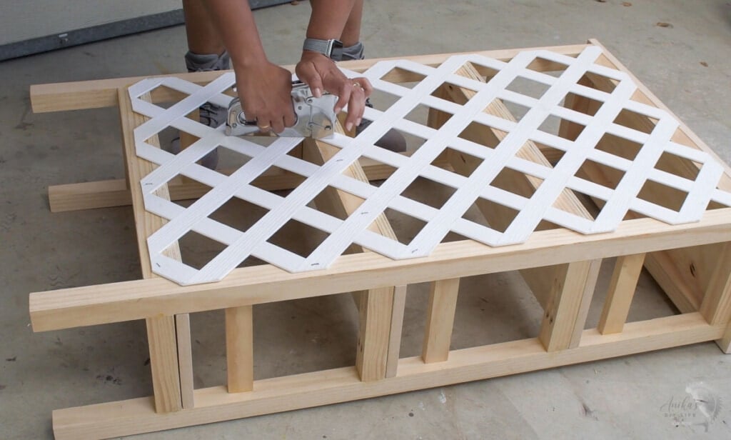 woman stapling vinyl trellis to the back of a bookshelf