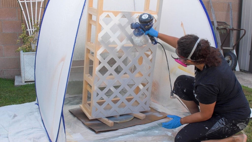 Woman spraying paint on a DIY trellis bookshelf