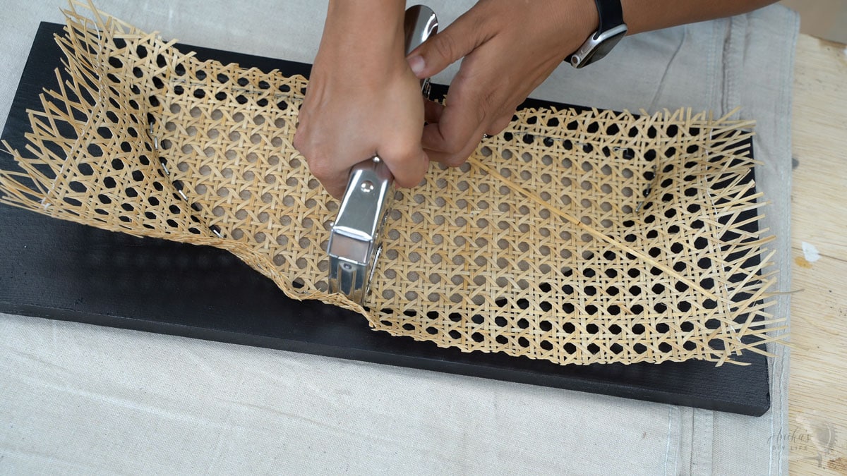 Woman using staple gun all around the drawer face cut out to attach cane webbing