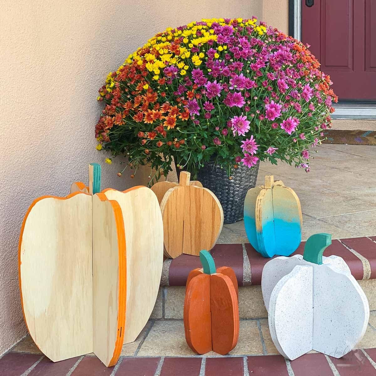 Five DIY plywood pumpkins sitting on the steps of the front porch