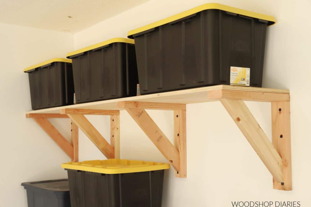 DIY wall mounted garage shelves with black totes on them.