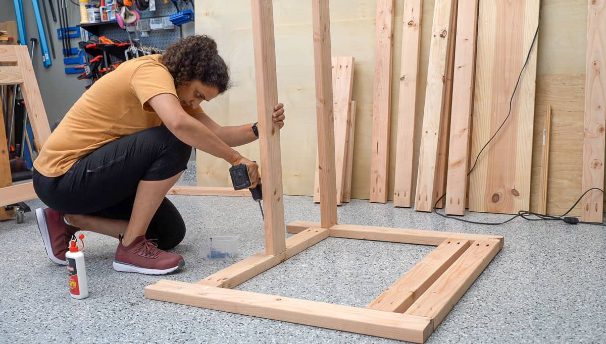 Woman attaching a long board to the leg frame of the workbench on the workshop floor