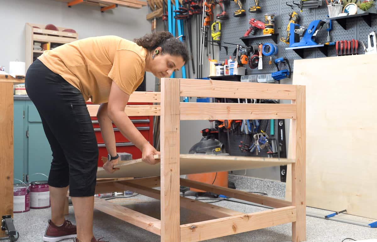 Woman adding a shelf to the bottom of the workbench
