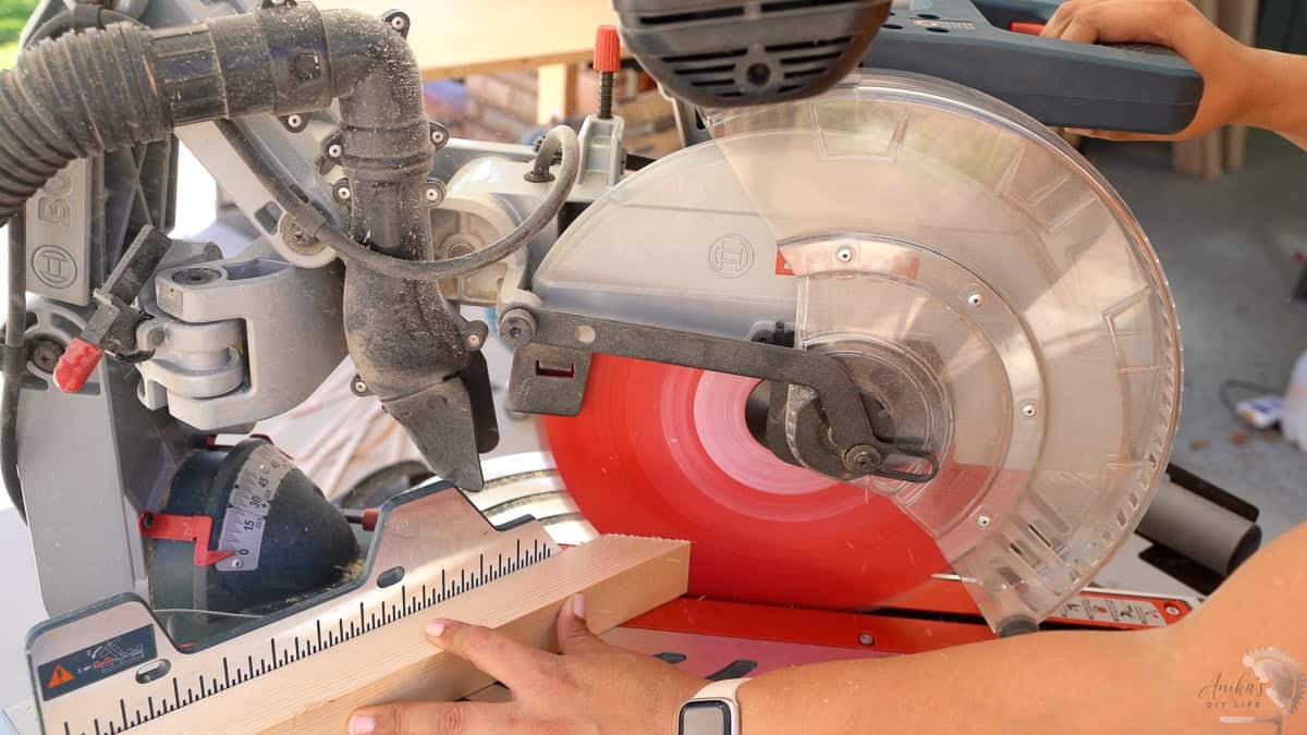 cutting a 45-degree miter with a miter saw to make a roof on the house shaped lantern