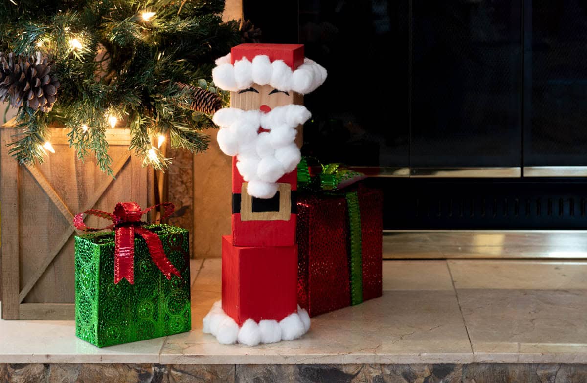 Finished DIY wood block Santa sitting next to presents and a Christmas tree