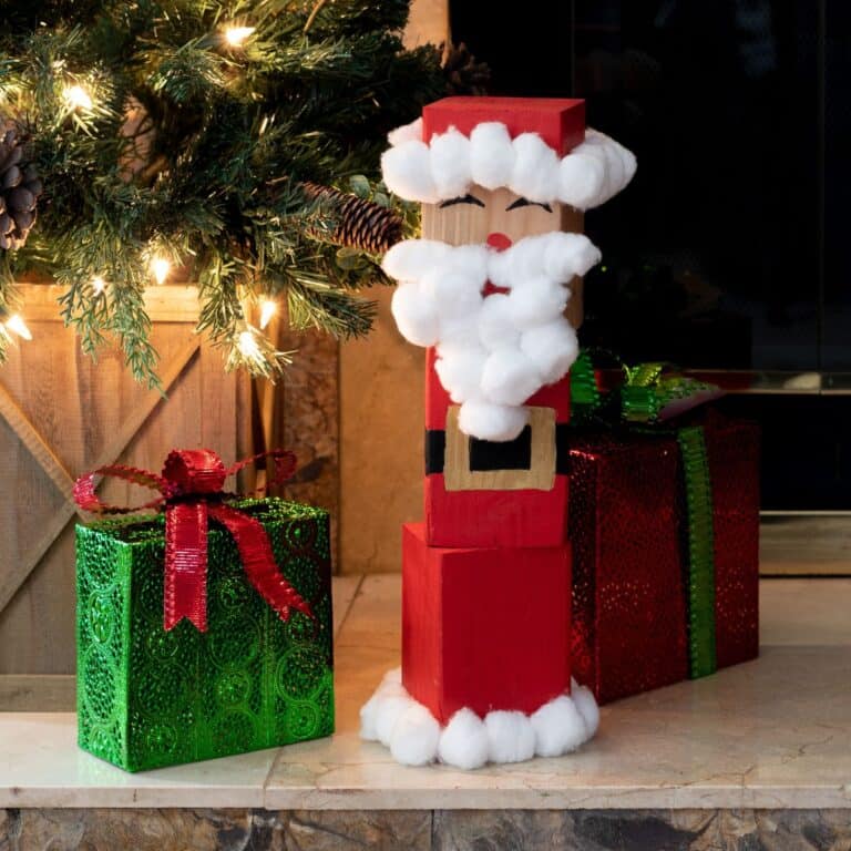 DIY wood block Santa sitting next to presents and a Christmas tree