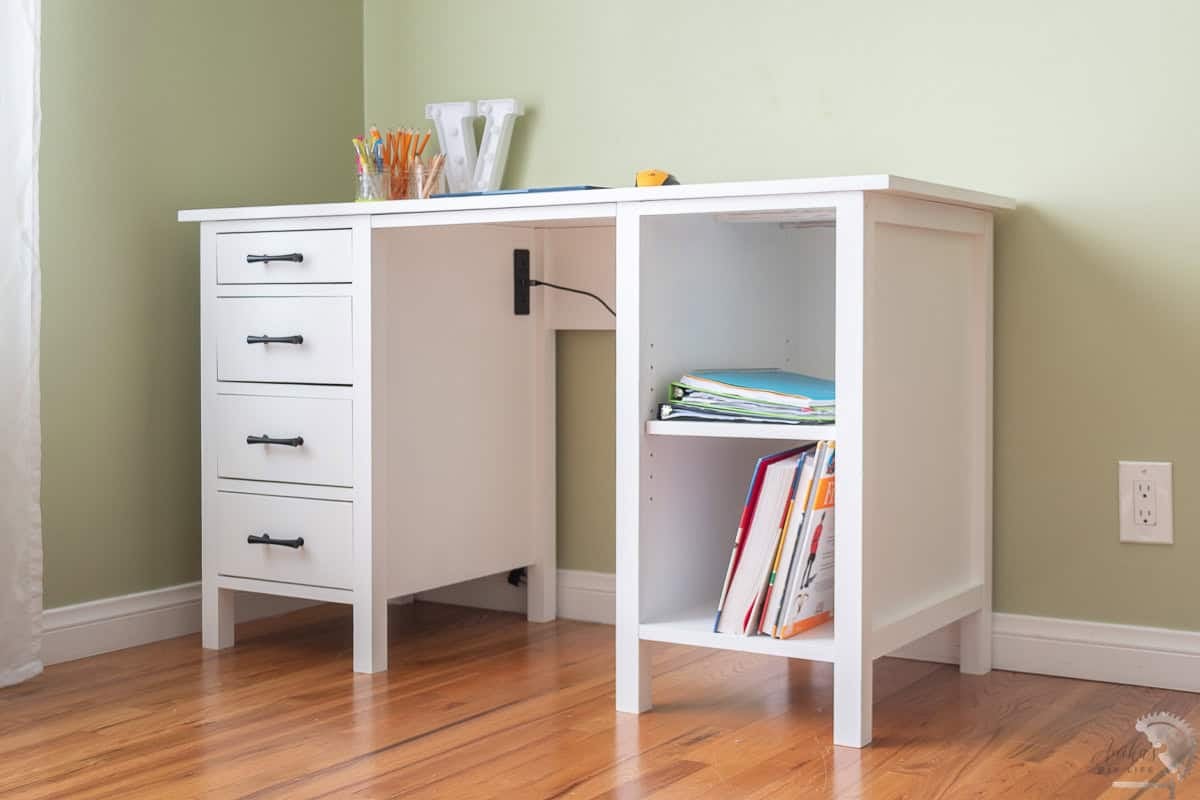 A white handmade wooden desk with four black drawer pulls and two open shelves on a wood floor.