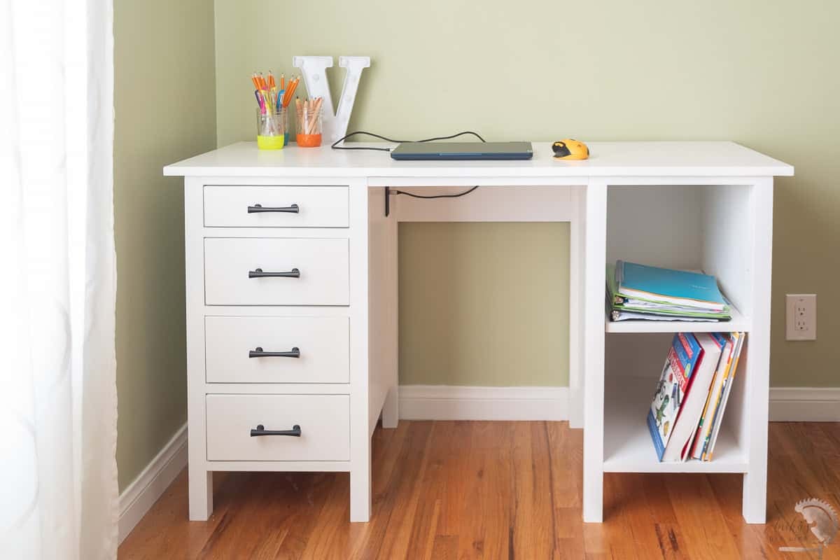 Front view of A white handmade wooden desk with four black drawer pulls and two open shelves on a wood floor.