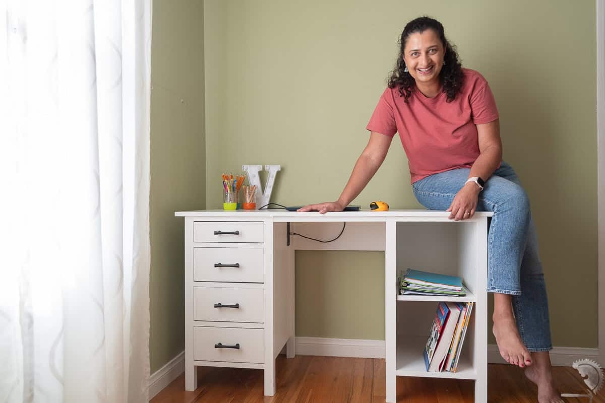 Anika with the white handmade wooden desk with four black drawer pulls and two open shelves on a wood floor.