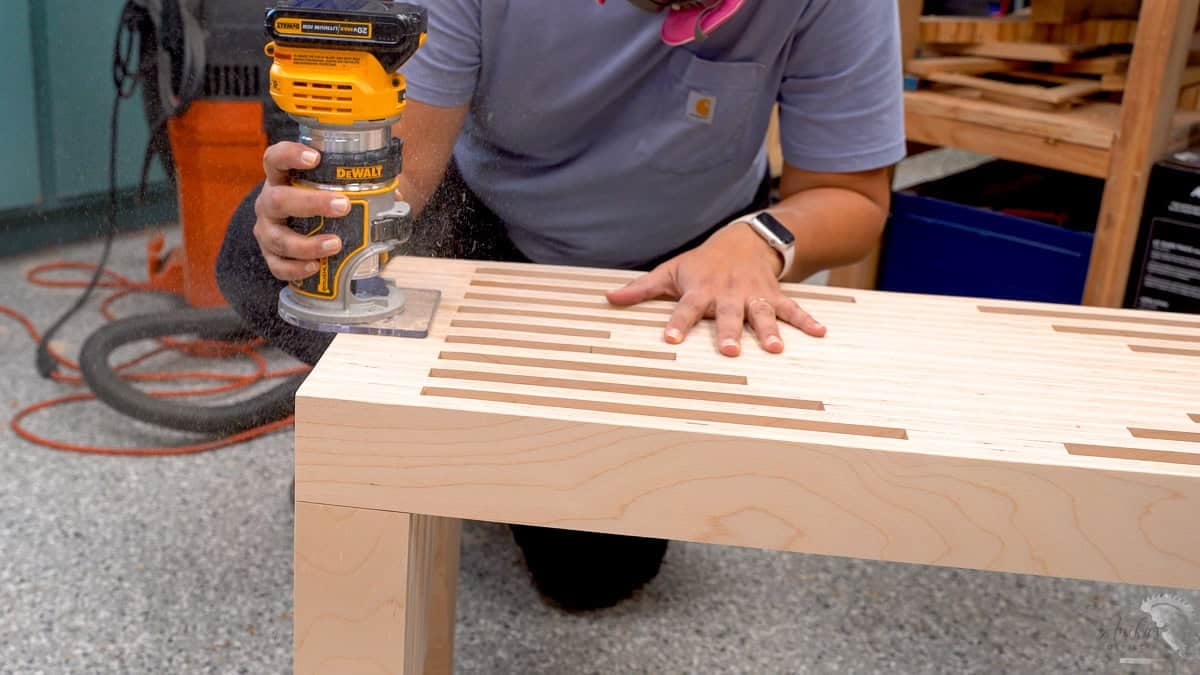 Anika using a dewalt router to soften the edge of the plywood bench