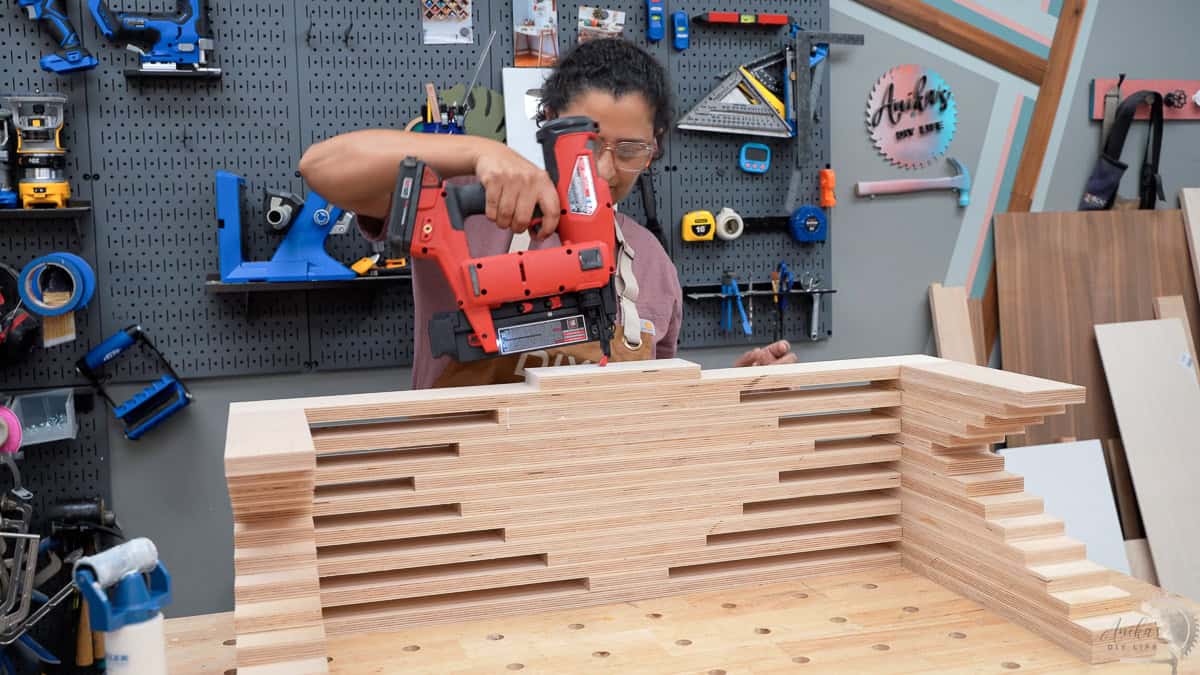 Anika attaching the final layers of the plywood bench with a nail gun on her workbench in a worshop