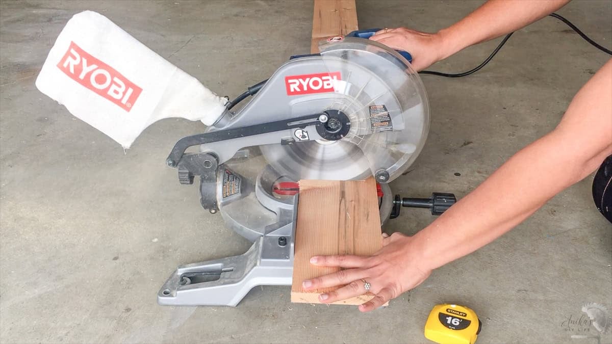 A beginner woodworker using a Ryobi compound miter saw to make an accurate crosscut on a wooden board.