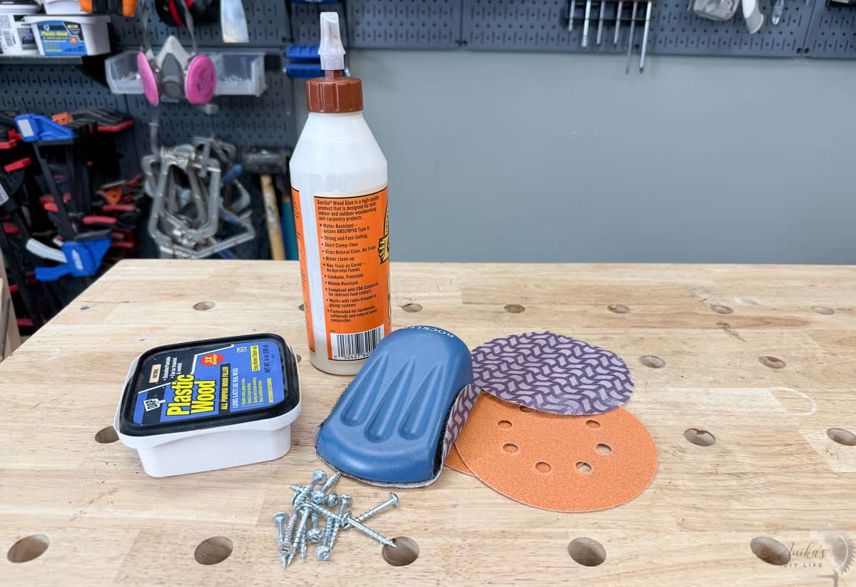 Woodworking consumables for beginners featuring Gorilla Wood Glue , wood filler , a variety of wood screws , sandpaper discs for a random orbital sander , and a hand sanding block