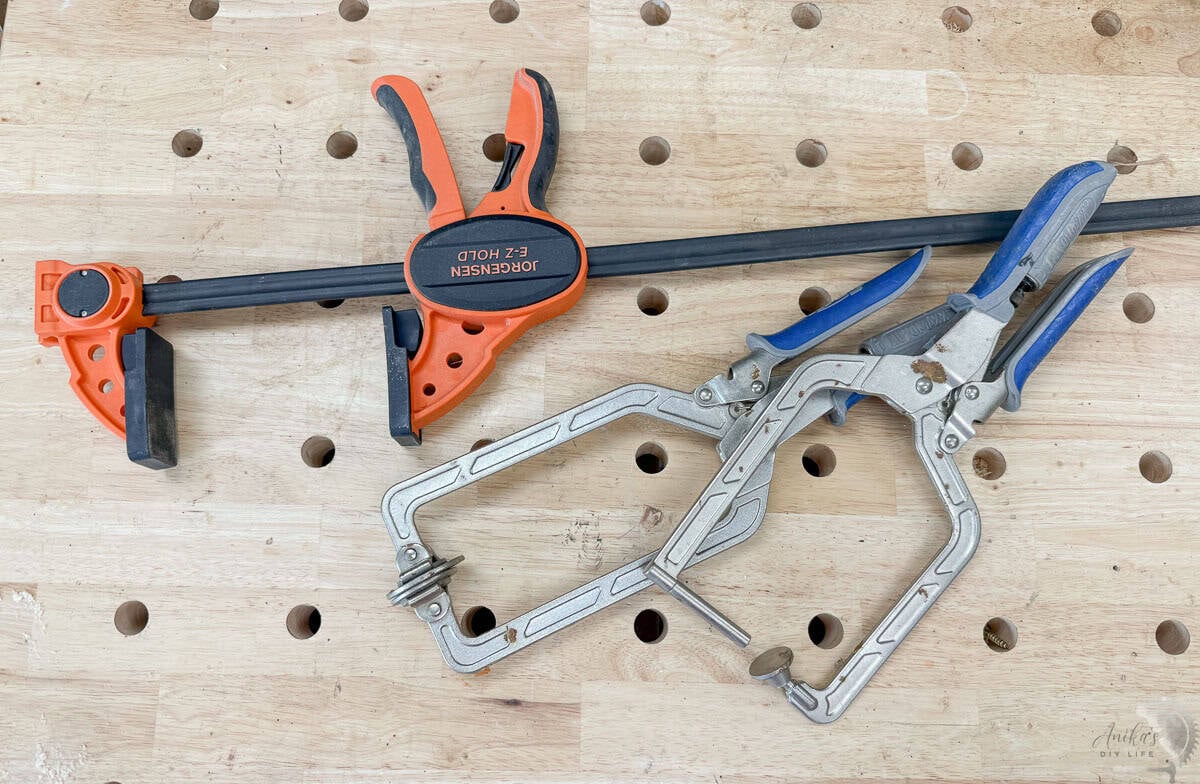 Essential woodworking clamps for project assembly including an orange F-style trigger clamp and silver right-angle pocket hole clamps