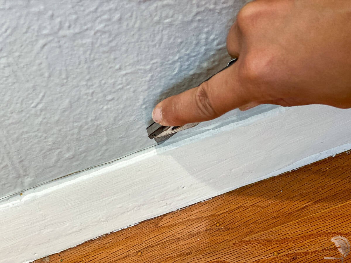 cutting the old caulk off of the baseboards with a utility knife