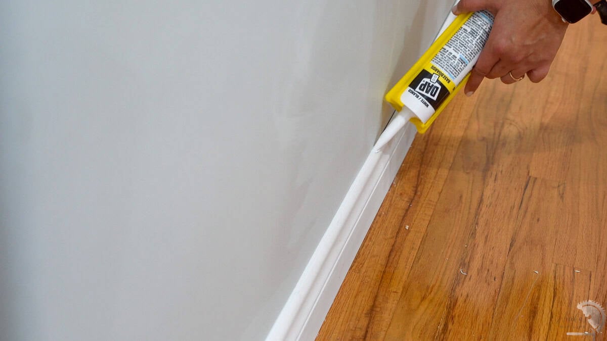 Applying caulking to the baseboards for a professional and seamless look.