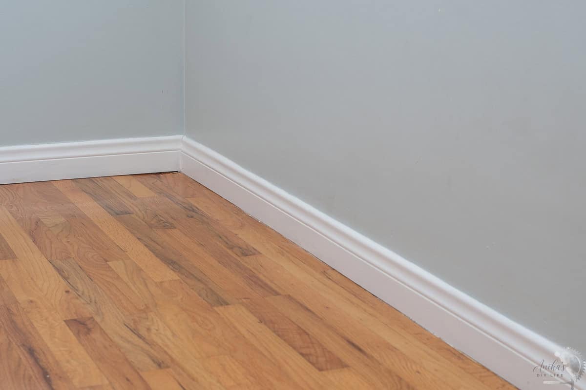 Beautiful white modern baseboards in a green room with wood floors
