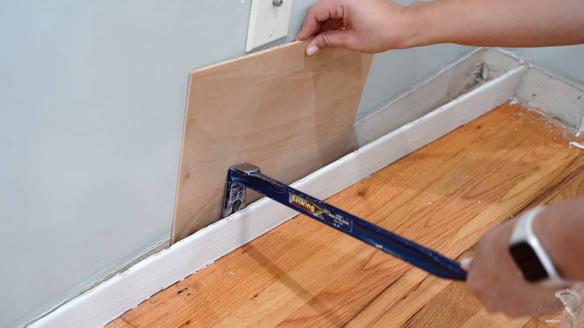 Pulling out the old baseboard with a scrap wood behind to protect the wall