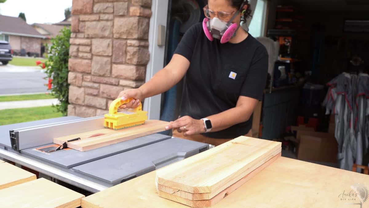Anika ripping cedar boards on the table saw with a yellow gripper.