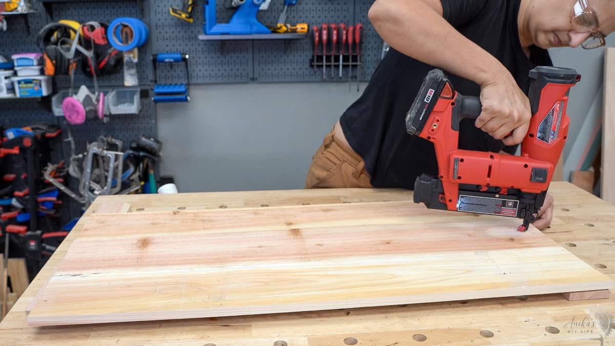 Anika Attaching cedar boards to build a panel for the planter box using a red brad nailer