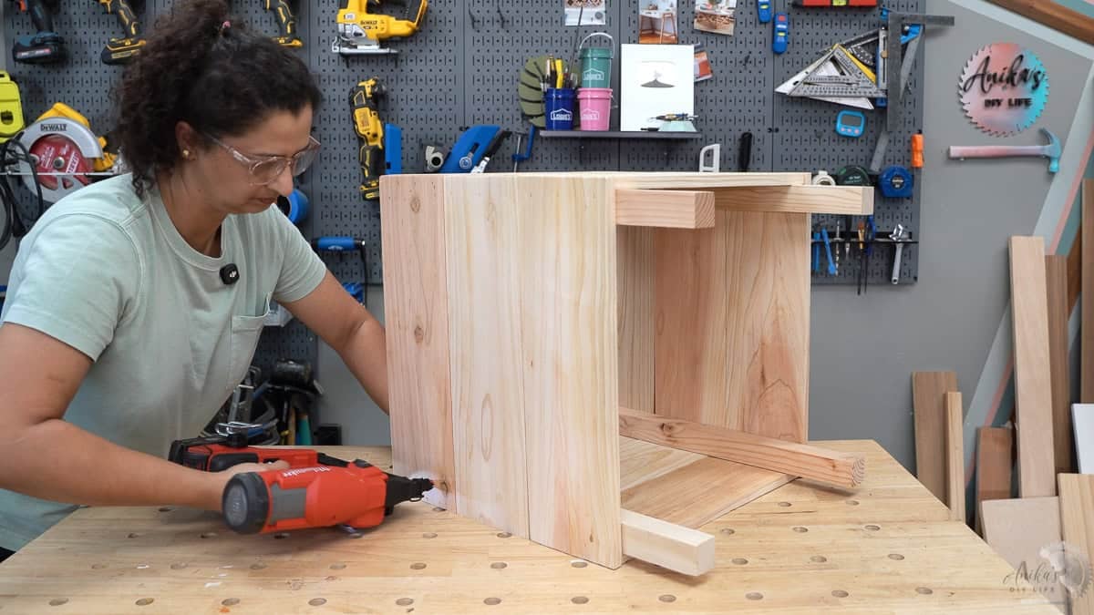 Anika finalizing the four-sided frame of the cedar planter box using a cordless nailer on a workbench