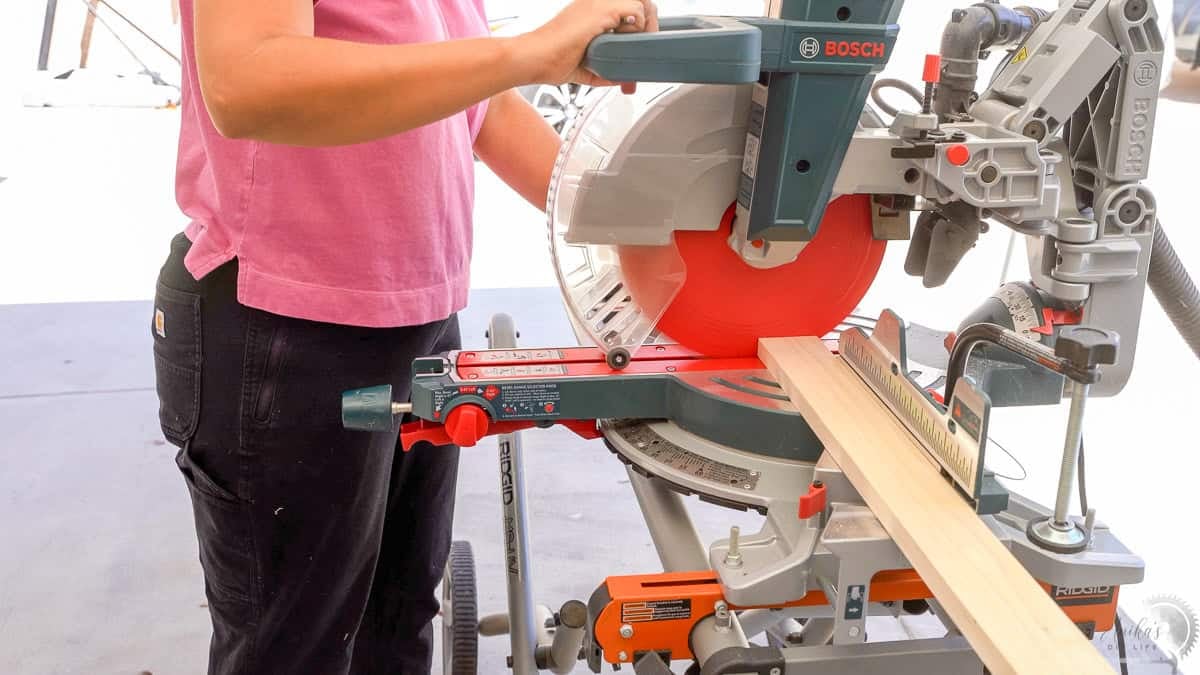 Anika cutting down boards for the DIY floating shelves on a miter saw