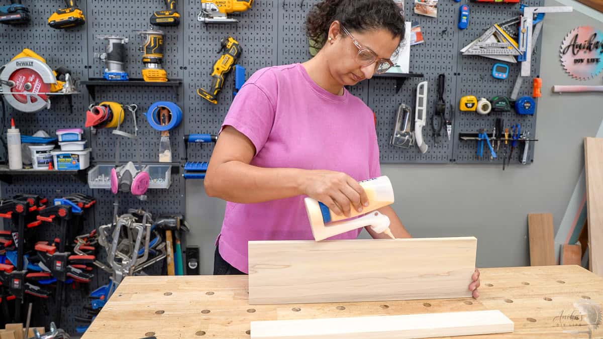 Applying wood glue to the edge of the board to build DIY floating shelves