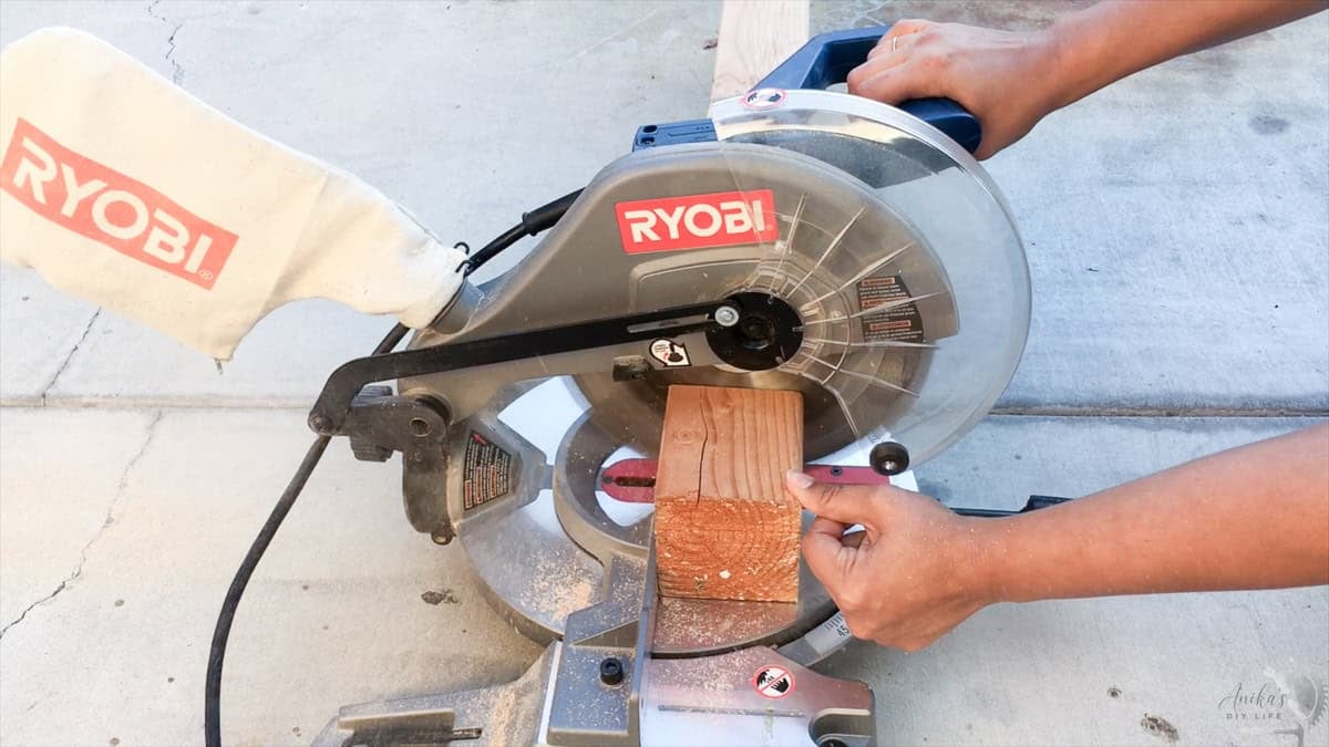Anika Using a 8" ryobi miter saw to cut a board on the floor