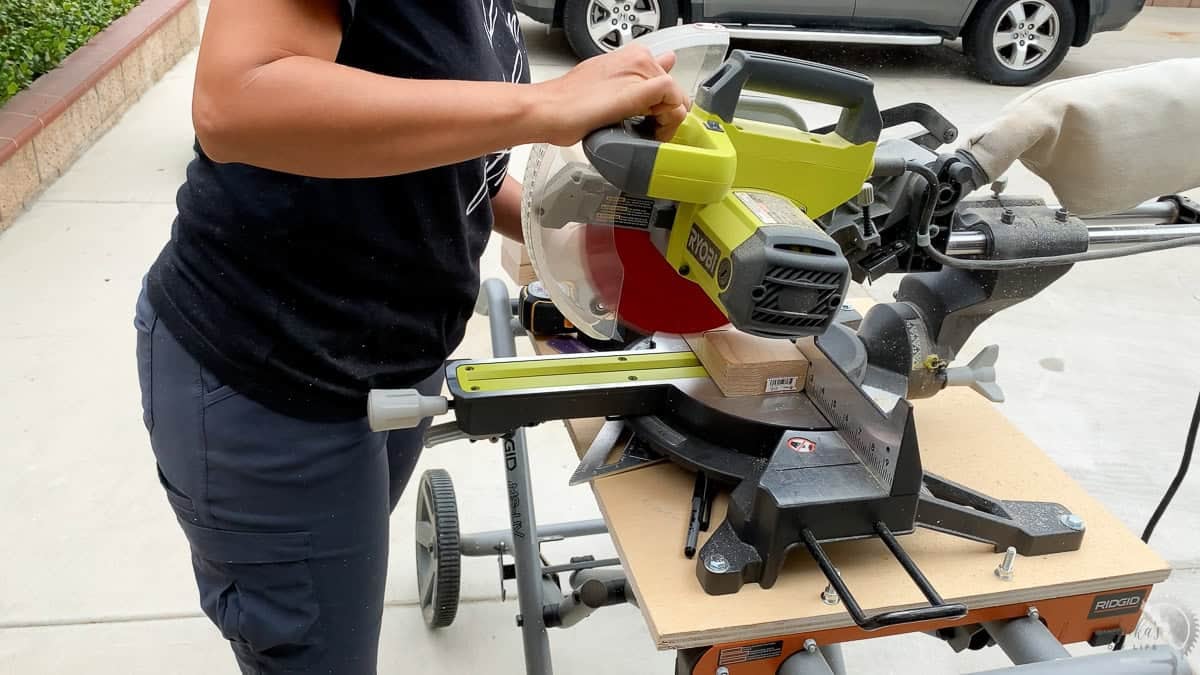 Anika using a 10" sliding Ryobi miter saw to cut wood boards