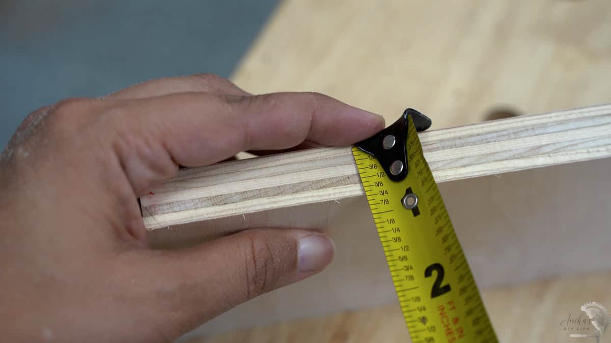 measuring the edge of plywood using a yellow measuring tape to show that it is indeed thinner than 3/4"