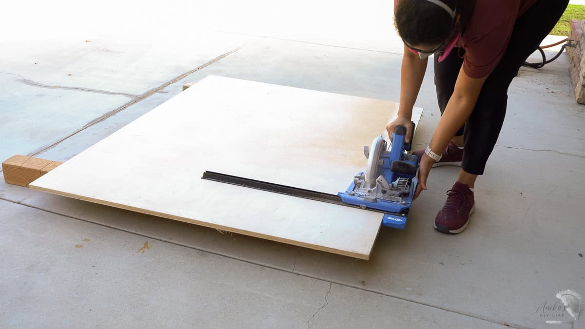 cutting plywood on the ground using a circular saw and a straight edge guide
